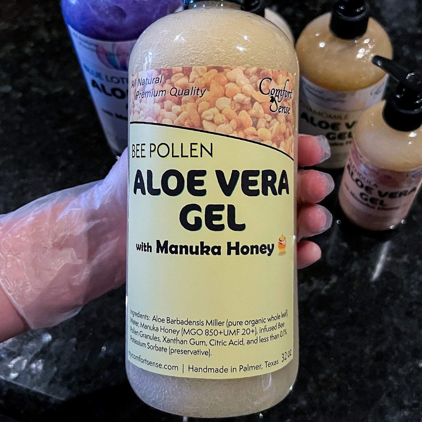 Bottle of Aloe Vera Gel with Manuka Honey held by a gloved hand on a dark surface.