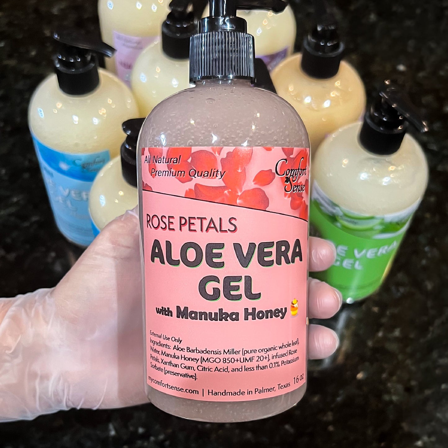 Hand holding a bottle of aloe vera gel with a pink label, surrounded by other aloe vera products.