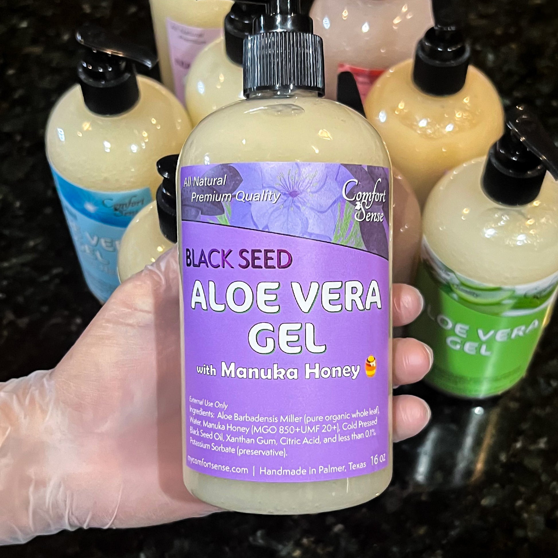 Hand holding a bottle of Black Seed Aloe Vera Gel with Manuka Honey, surrounded by other similar products.
