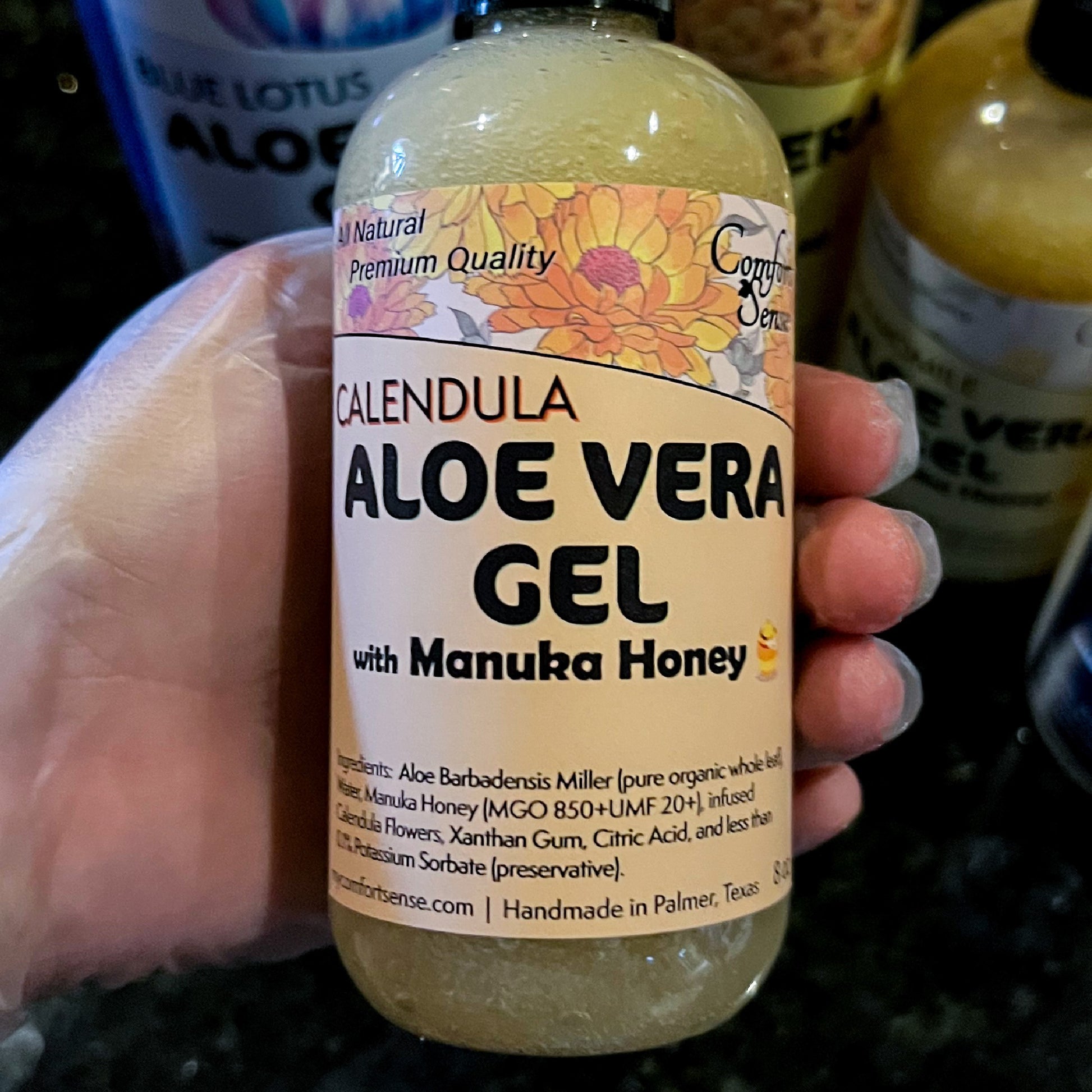 Bottle of Calendula Aloe Vera Gel with Manuka Honey held by a hand, with a blurred background.