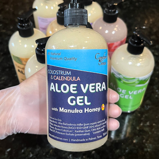 Bottle of aloe vera gel with colostrum and calendula held by a gloved hand, with more bottles in the background.