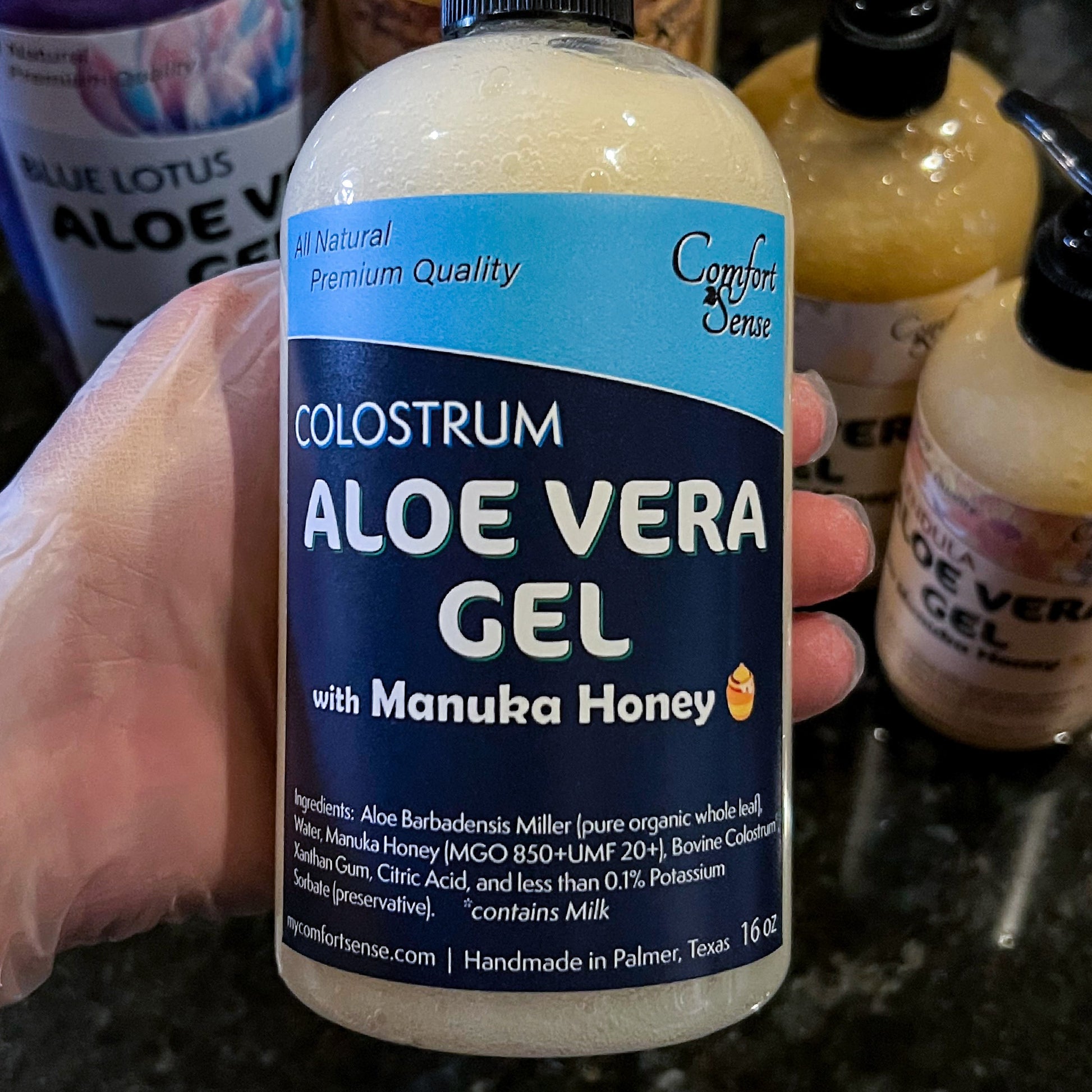 Bottle of Colostrum Aloe Vera Gel with Manuka Honey held by a gloved hand.
