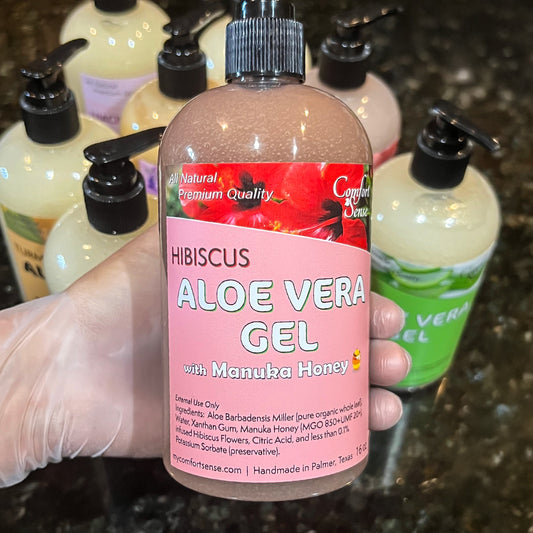 Bottle of hibiscus aloe vera gel with manuka honey held by a gloved hand, surrounded by other similar bottles.