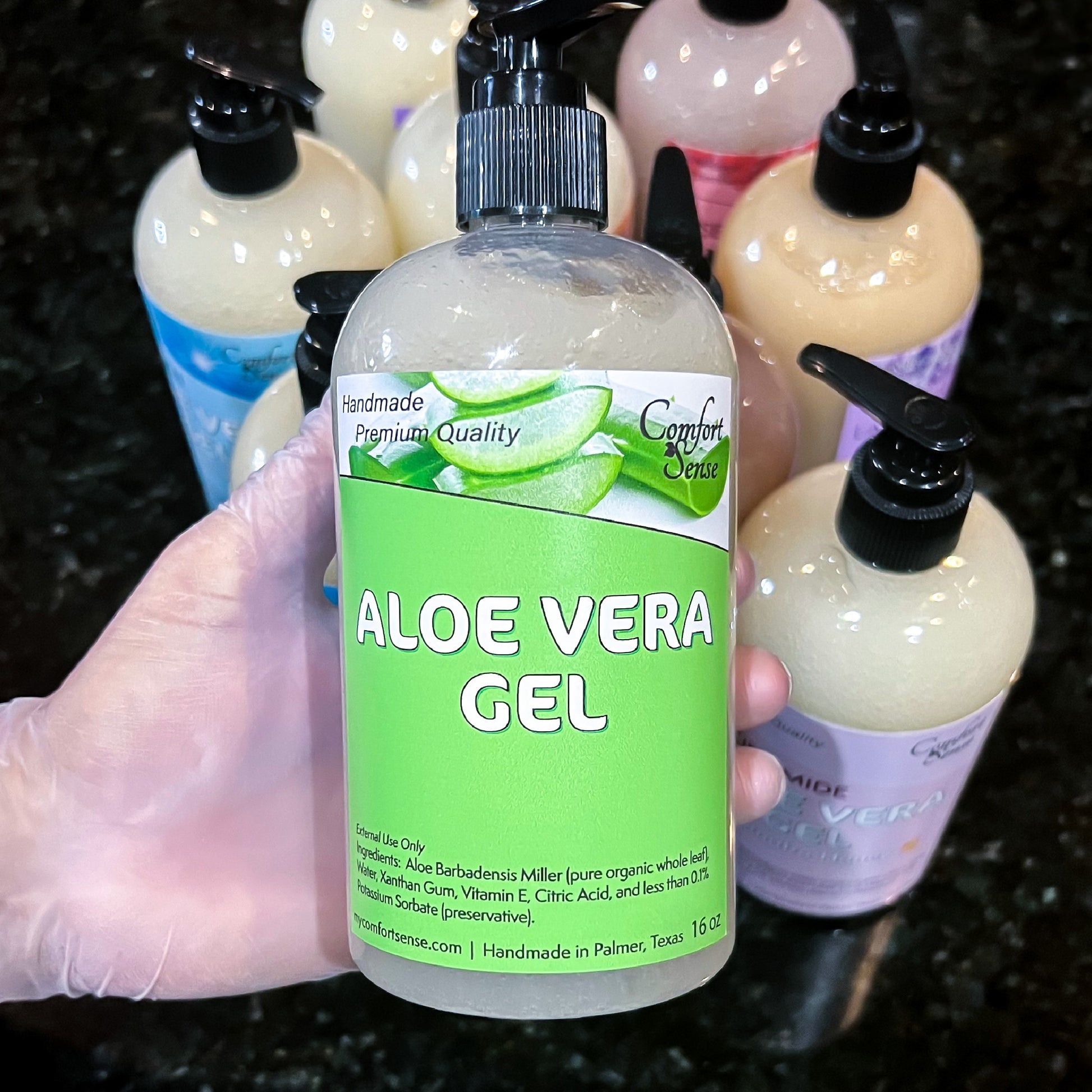 Bottle of Aloe Vera gel held by a gloved hand with more bottles in the background.