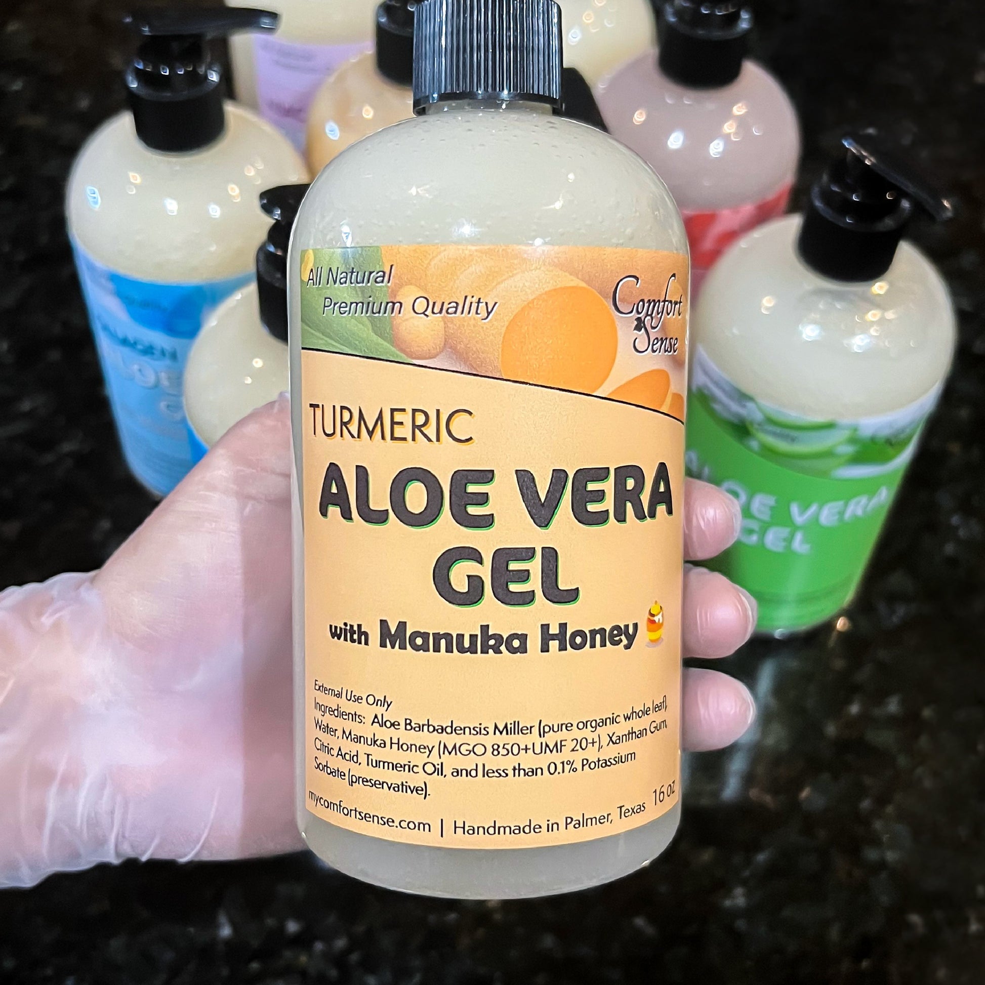 Bottle of Aloe Vera Gel with Turmeric and Manuka Honey held by a gloved hand, surrounded by other similar bottles.