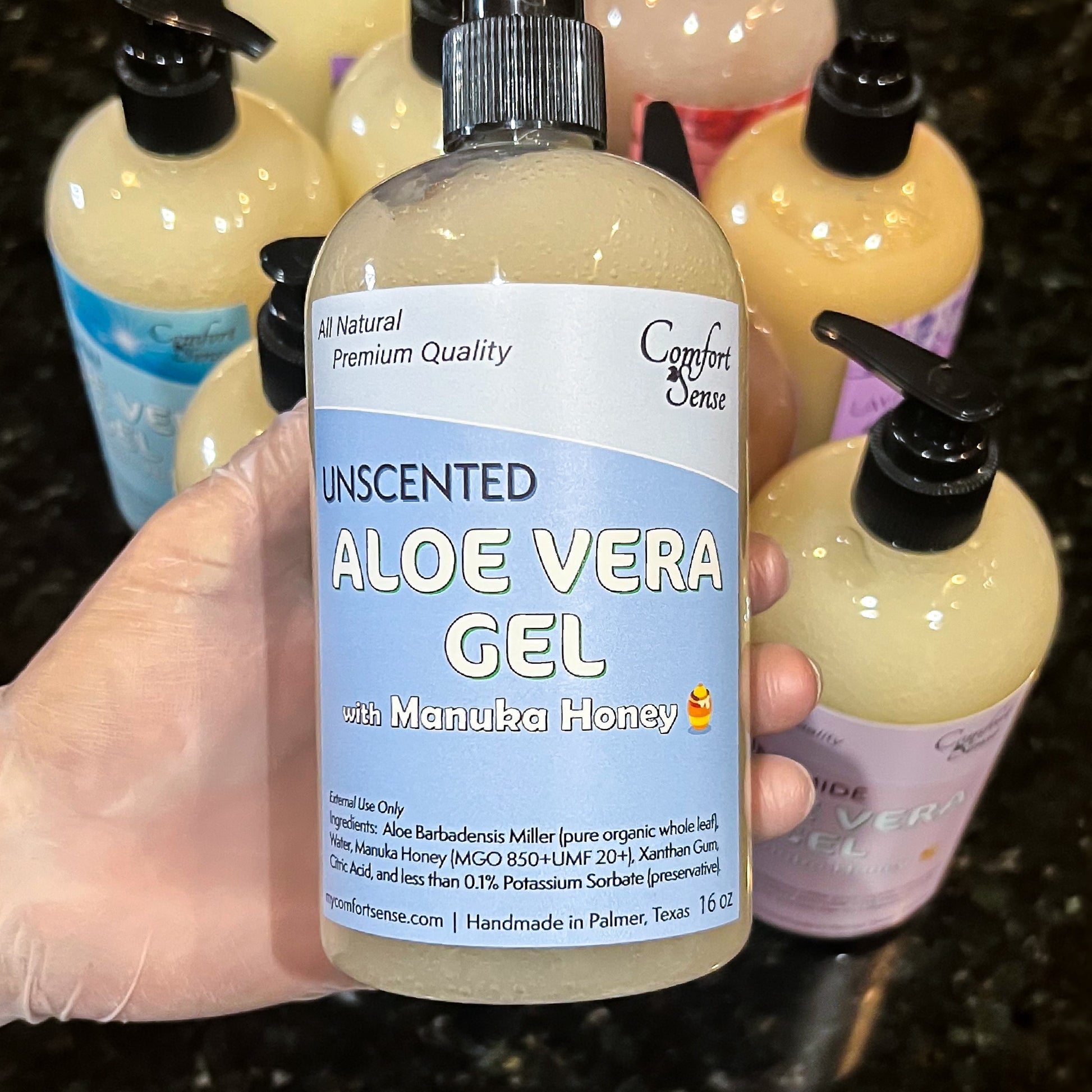 Hand holding a bottle of unscented aloe vera gel with manuka honey, surrounded by other skincare products.