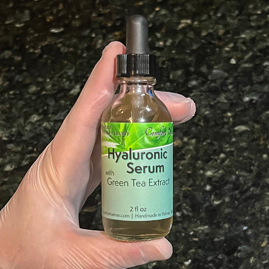 Hand holding a bottle of hyaluronic serum with green tea extract against a dark background